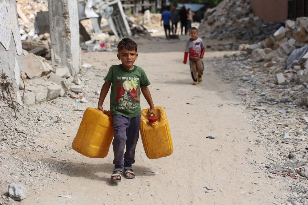 Displaced Palestinian youths carry containers to ferry water from a distribution point in the Shujaiya neighbourhood of Gaza City on Monday