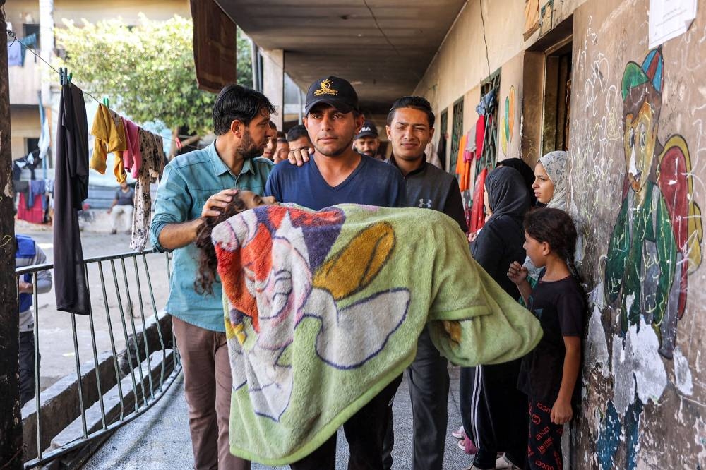 A man carries the blanket-wrapped body of a girl who was killed in bombardment on the Rafei school serving as a displacement shelter in the Jabalia camp for Palestinian refugees in the northern Gaza Strip on Wednesday. AFP