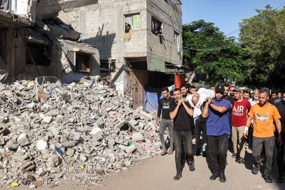 Mourners carry the body of Hussam al-Khalidi, who was killed in Israeli bombardment at his family home in the Bureij camp for Palestinian refugees in the central Gaza Strip, as they march past a collapsed building during his funeral in Bureij on Wednesday. AFP
