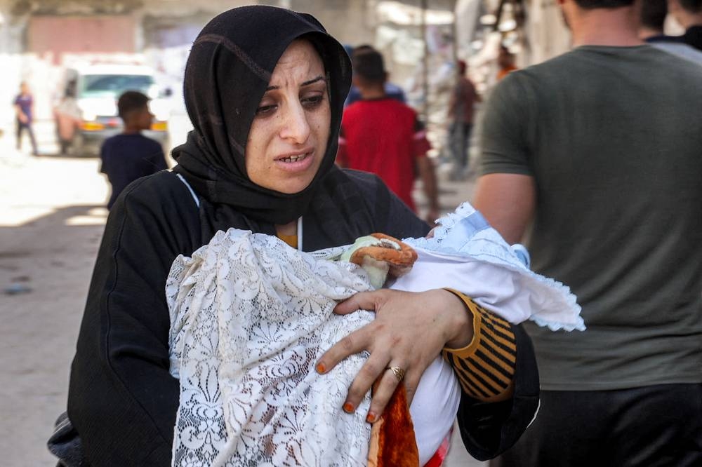 An evacuating woman walks carrying an infant child in the Jabalia camp for Palestinian refugees in the northern Gaza Strip on Wednesday. AFP