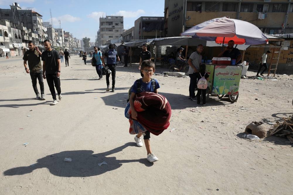 A child carries belongings as displaced Palestinians make their way to flee areas in the northern Gaza Strip in Gaza City on Saturday. REUTERS
