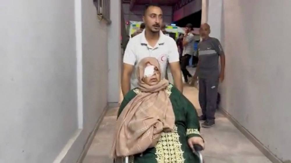 A member of the Palestine Red Crescent Society assists a wounded Palestinian person in a wheelchair, during the evacuation of people from Kamal Adwan Hospital in northern Gaza to Al-Shifa Hospital in Gaza City. Palestine Red Crescent Society/Handout via REUTERS