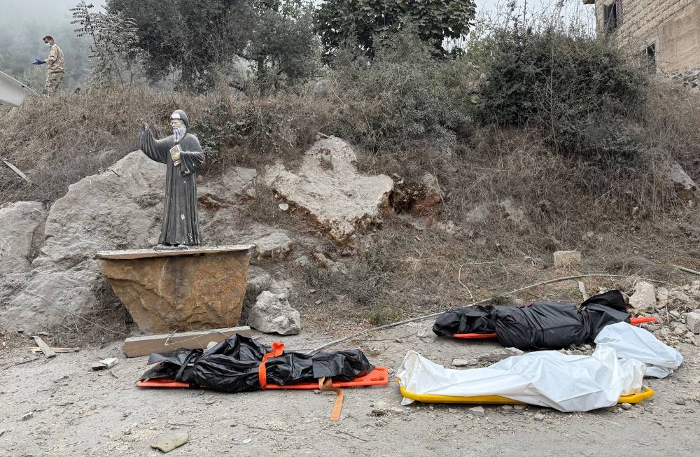 Dead bodies lie on the ground in bodybags near a statue of Saint Charbel, at a site of an Israeli air strike in the Christian-majority region of Aitou in north Lebanon, on Monday. REUTERS