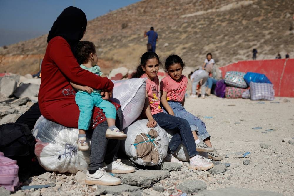 People wait for further transportation after crossing the damaged part of the road at the Masnaa border crossing, on Monday. REUTERS