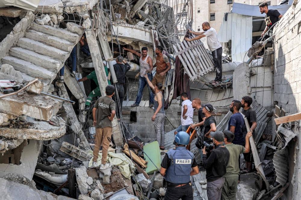 People gather outside a collapsed building as they attempt to extricate a man from underneath the rubble following Israeli bombardment in the Saftawi district in Jabalia in the northern Gaza Strip on Tuesday. AFP