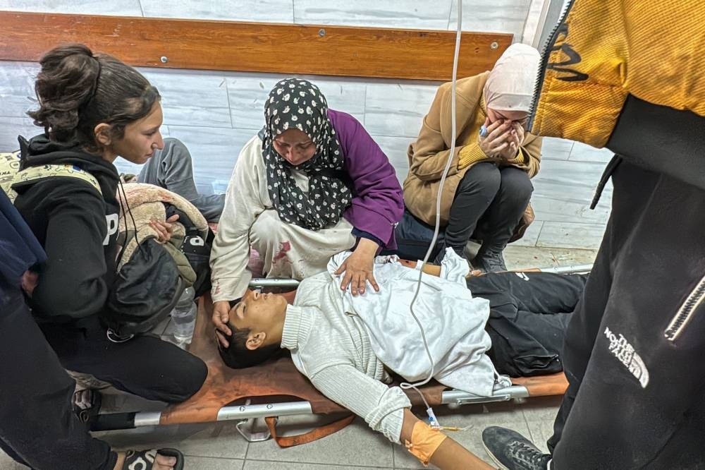 A Palestinian family sits by a youth injured in Israeli bombardment of the Beit Lahia Project, as he receives first aid on the floor of the Kamal Adwan Hospital emergency hall in Beit Lahia in the northern Gaza Strip on Wednesday. AFP