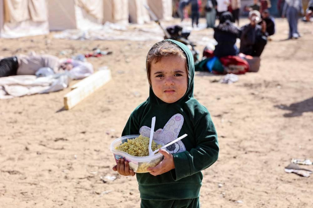 A displaced Palestinian child who fled with family members Israeli army operations in the northern Gaza Strip, carries a bowl of food in front of a newly set up tents at the Yarmouk Sports Stadium, once a football arena, in Gaza City on October 25, 2024, amid the ongoing war between Israel and the Palestinian Hamas group. (Photo by Omar AL-QATTAA / AFP)