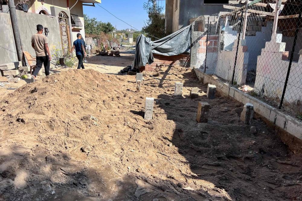 People walk past makeshift graves marked with concrete blocks for people killed in Israeli strikes a day earlier in Beit Lahia, in the northern Gaza Strip, on Wednesday. AFP