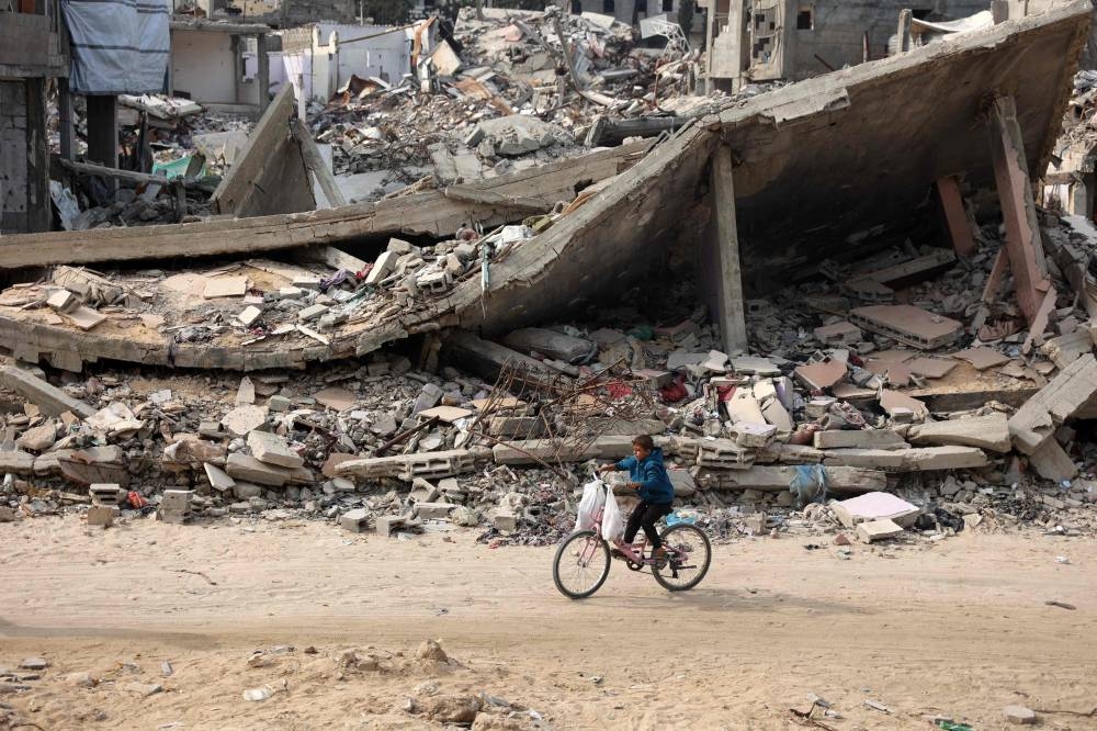 A Palestinian child rides his bicycle past a levelled building in Gaza City on Saturday. AFP
