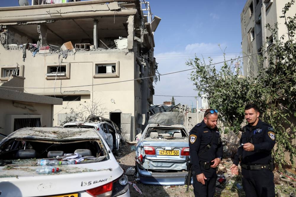 Police officers stand near damaged cars and a house that was hit, following a projectiles attack from Lebanon towards Israel, in the central Israeli town of Tira, on Saturday. REUTERS