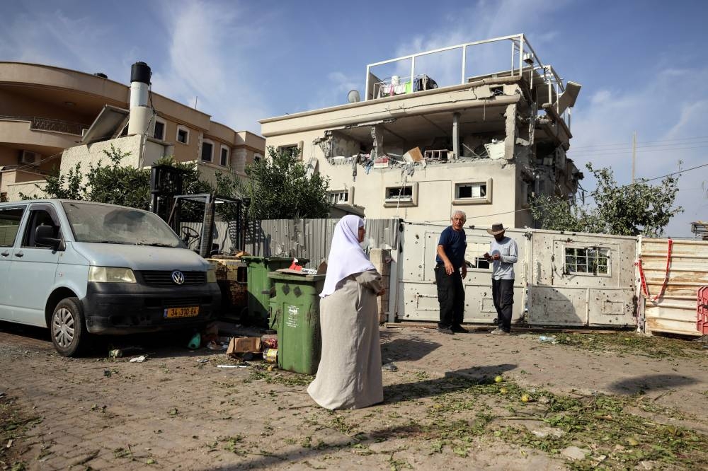 People stand near a house that was hit, following a projectiles attack from Lebanon towards Israel, in the central Israeli town of Tira, on Saturday. REUTERS