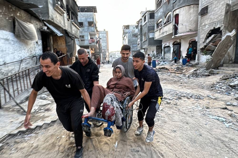 Palestinians use a wheelchair to transport through the streets a woman who lost her leg when her family home was hit in an Israeli strike in the Jabalia refugee camp in the northern Gaza Strip, on Thursday. AFP