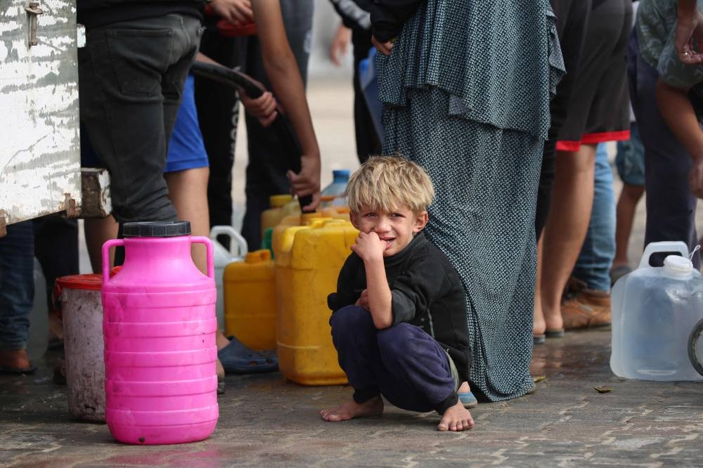 A displaced Palestinian child sits waiting as people fill containers with clean water, at the al-Bureij refugee camp in the central Gaza Strip, on Sunday. AFP