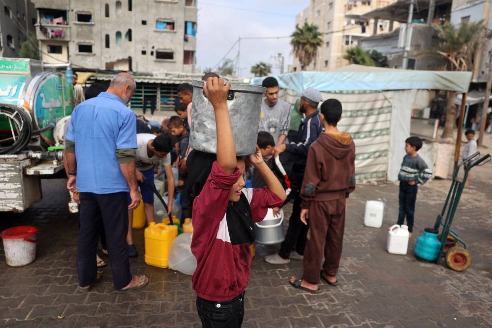 A displaced Palestinian child carries a pot filled with clean water above her head at the al-Bureij refugee camp in the central Gaza Strip, on Sunday. AFP