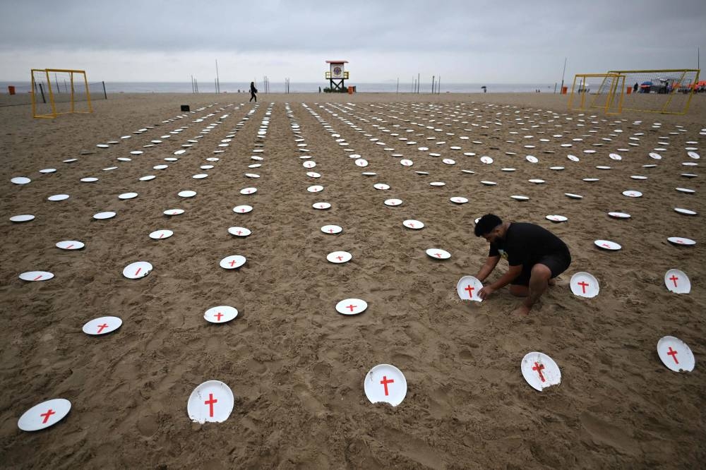 An activist from the human rights group Rio de Paz places one of 733 plates with a red cross in the sand on Copacabana beach in Rio de Janeiro, Brazil, on Saturday, ahead of the G20 Summit to urge world leaders to tackle hunger. The empty pleates represent the 733 million people in the world suffering hunger according to UN data. AFP