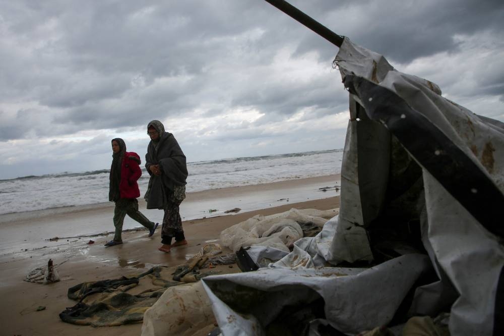 Displaced Palestinians walk past a damaged tent following rising sea levels and heavy rainfall, in Khan Younis in the southern Gaza Strip, on Monday. REUTERS
