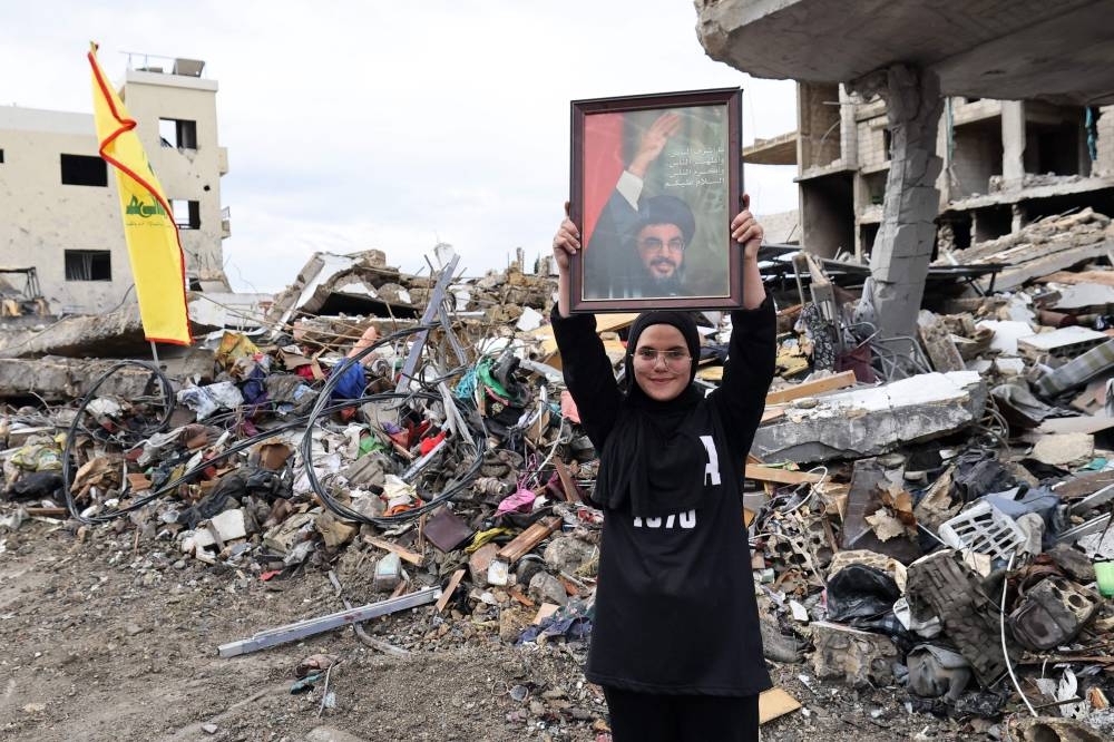 A resident of the southern Lebanese village of Zibqin raising a picture of slain Hezbollah leader Hassan Nasrallah, stands amid the destruction on November 27, 2024, as people who had fled the war between Israel and Hezbollah returned to check on their homes, on Wednesday. AFP