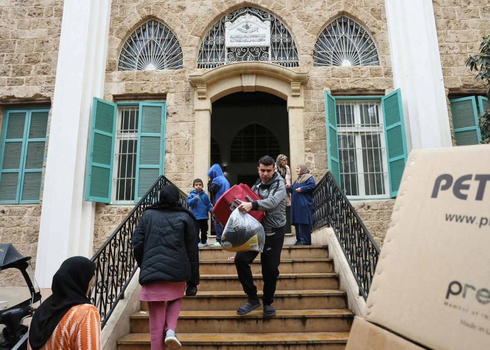 Displaced people carry their belongings as they leave a school turned shelter in Beirut, as people return to their homes after a ceasefire between Israel and Hezbollah took effect, on Wednesday. AFP