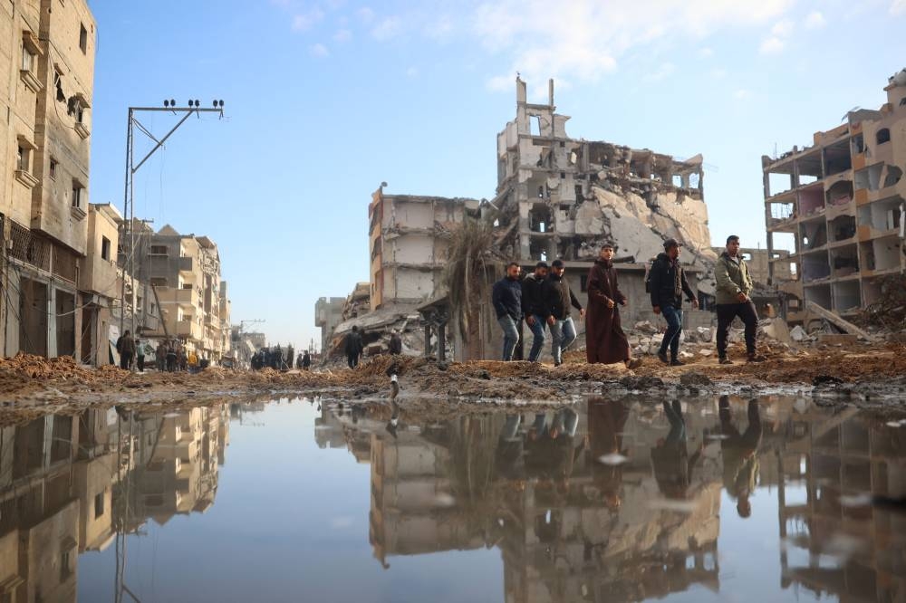 Palestinian men walk past stagnant water amid destroyed buildings in Nuseirat in the central Gaza Strip as residents of the camp returned to check their homes after Israeli shelling stopped, on Friday. AFP