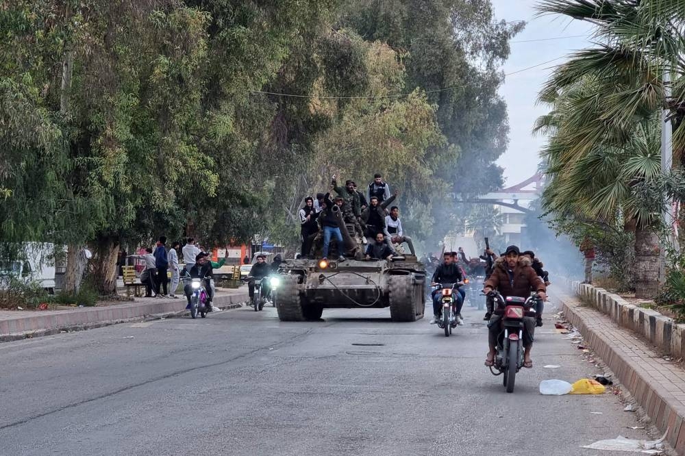 People ride a tank in the Syrian southern city of Daraa on Saturday after the collapse of government forces. AFP