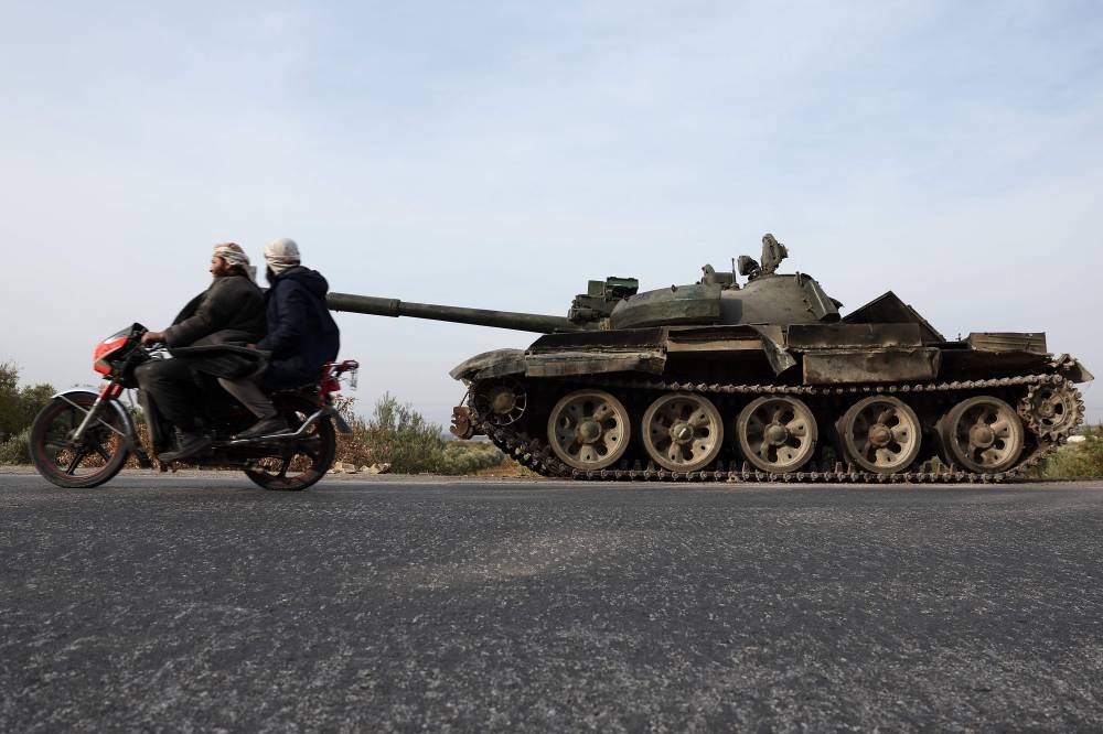 Men ride a motorcycle past a military vehicle belonging to the Syrian regime forces abandoned on the side of a road in the Hama governorate after anti government forces took control of the area, on Saturday. AFP