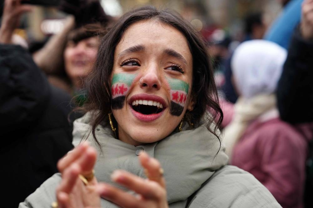 A woman, with an opposition flag painted on her face, applauds as members of the Syrian community and supporters gather to celebrate the fall of Syrian president Bashar al-Assad in the face of an offensive by Islamist-led rebels, in Paris, on Sunday. AFP