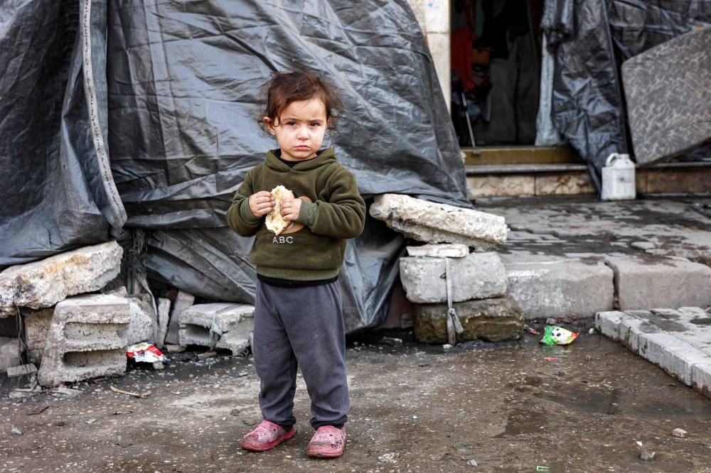 A child holds a half-eaten piece of bread while standing outside a tent at a shelter for displaced Palestinians in Gaza City, on Wednesday. AFP