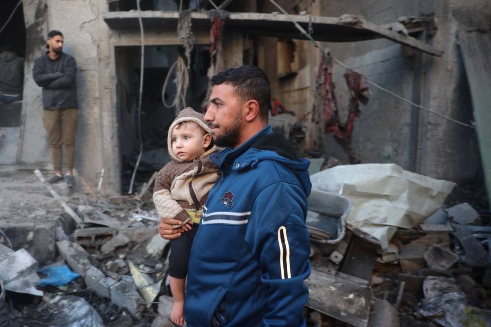A Palestinian man carrying a child walks past a destroyed building in the Nuseirat refugee in the central Gaza Strip on Friday. AFP