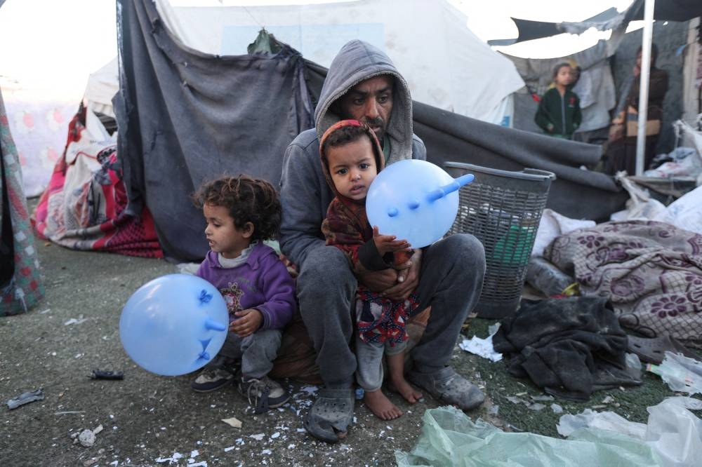 A man sits with two children, as Palestinians inspect the damage at a tent camp sheltering displaced people, following an Israeli strike, in Deir Al-Balah in the central Gaza Strip, on Sunday. REUTERS