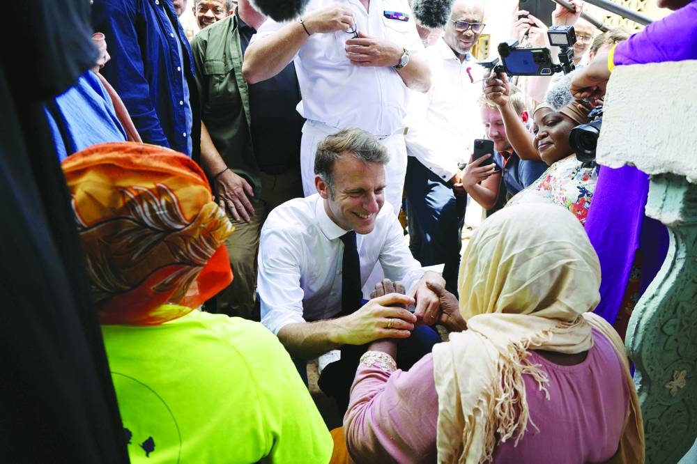 France's President Emmanuel Macron holds hands of a local resident during his visit to a neighbourhood in Tsingoni, on the French Indian Ocean territory of Mayotte on December 20, 2024, following the cyclone Chido's passage over the archipelago. Distraught and angry inhabitants of Mayotte shouted out their despair to French President Emmanuel Macron during his visit on December 19, five days after the Indian Ocean archipelago was devastated by a cyclone, with lacking water and food, and fear of looting topping the grievances. (Photo by LUDOVIC MARIN / POOL / AFP)