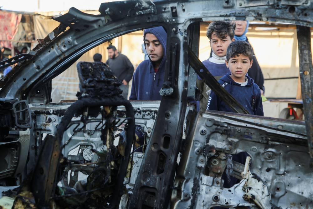 Palestinian children inspect the remains of a car in the aftermath of an Israeli strike, in Khan Younis in the southern Gaza Strip Monday