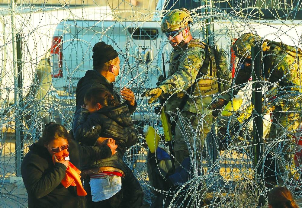 
Migrants react near a razor wire fence, set by US to inhibit the crossing, after a member of the Texas National Guard fired tear gas, as seen from Ciudad Juarez, Mexico, on December 19. 