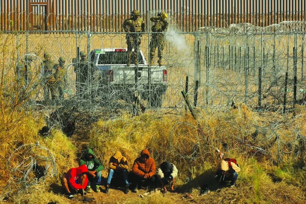 
FILE PHOTO: Migrants sit near a razor wire fence, set by US authorities to inhibit the crossing, as a member of the Texas National Guard aims to fire tear gas in Ciudad Juarez, Mexico, on December 18. 