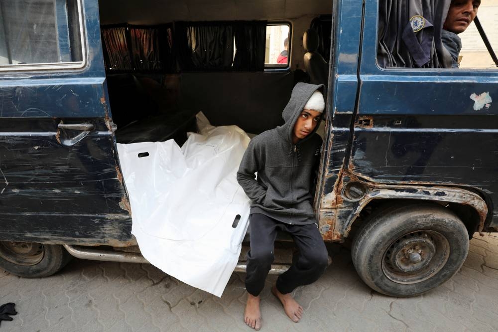 A mourner sits next to the body of a Palestinian killed in Israeli airstrikes during their funeral, in Gaza City, on Friday. REUTERS