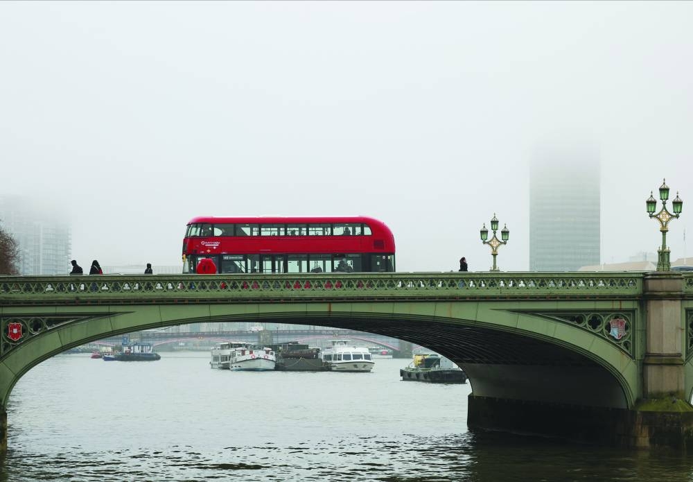 
A double-decker red bus drives across Westminster Bridge during foggy weather. 
