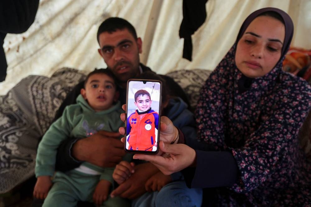 Asmaa, the mother of 9-year-old Palestinian boy Ramadan Hamed, who doctors said died due to malnutrition, displays a picture of him on a mobile phone as she shelters inside a tent with her husband and children after being displaced from their home, in Nusierat in the central Gaza Strip on December 7. REUTERS