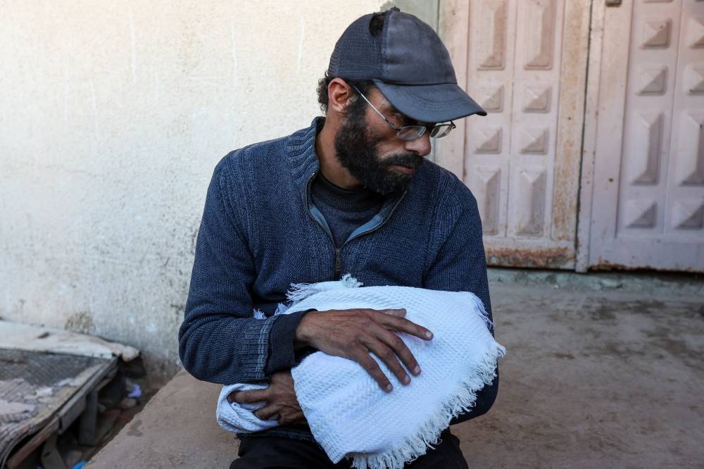 Yahya Al-Batran, the father of Palestinian infant Jumaa Al-Batran, who died of hypothermia after living in a tent with his displaced family, holds his body at Al-Aqsa Martyrs Hospital, in Deir Al-Balah in the central Gaza Strip, on Sunday. REUTERS
