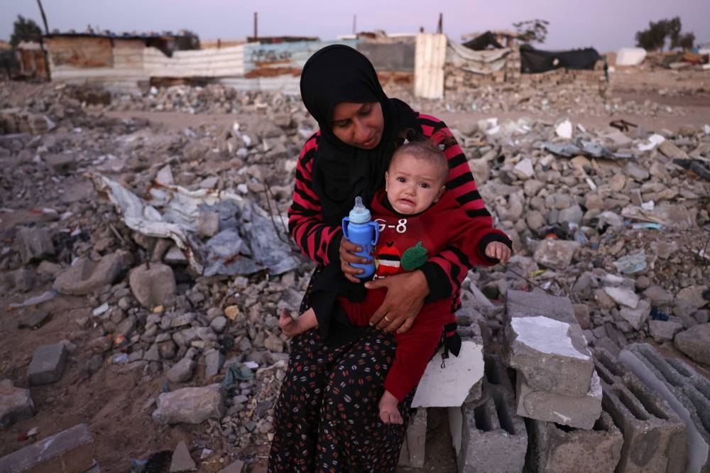 A woman feeds her child amid the rubble of destroyed buildings at a makeshift camp for displaced Palestinians in the Nahr al-Bared area in Khan Yunis, in the southern Gaza Stri. AFP