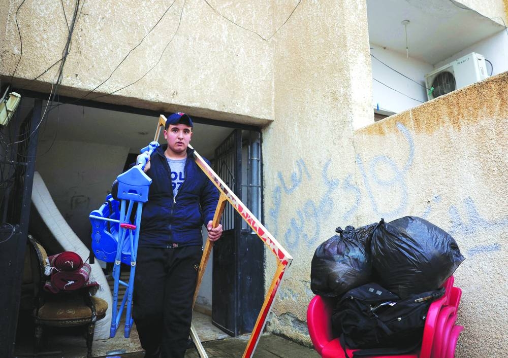 A member of the Assad regime's soldier family takes his family belongings out of an apartment next to a sign reading 'Faction of Amr ibn al-As', on the outskirts of Damascus following evacuation orders from factions of Hay'at Tahrir al-Sham (HTS), after Syria's Bashar al-Assad was ousted.