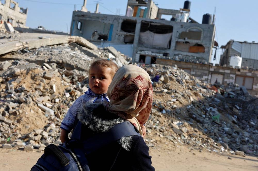 A Palestinian woman carrying a child walks past the rubble of a house, destroyed in previous Israeli strikes, in Khan Younis, southern Gaza Strip, on Tuesday. REUTERS