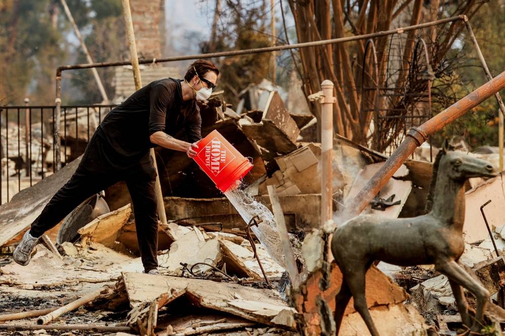 Chris Sullivan throws a bucket of water to douse an hotspot at a house that was burnt down by the Eaton Fire, on Friday. REUTERS