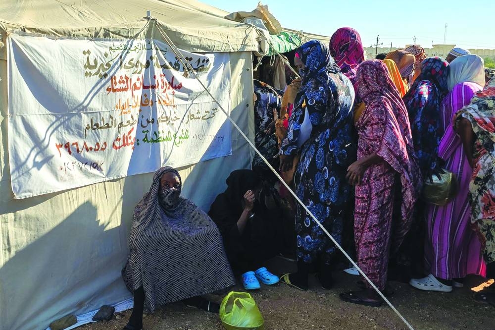 People wait to collect food at a location set up by a local humanitarian organisation to donate meals and medication to people displaced by the war in Sudan, in Meroe in the country's Northern State.