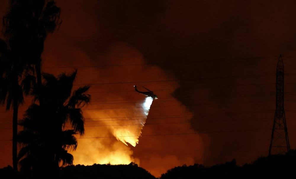 A firefighting helicopter drops water as the Palisades Fire burns toward the Mandeville Canyon neighbourhood in Los Angeles, California on Friday.