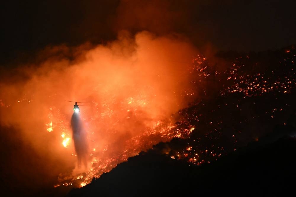 A fire fighting helicopter drops water as the Palisades fire grows near the Mandeville Canyon neighborhood and Encino, California, on Saturday. AFP