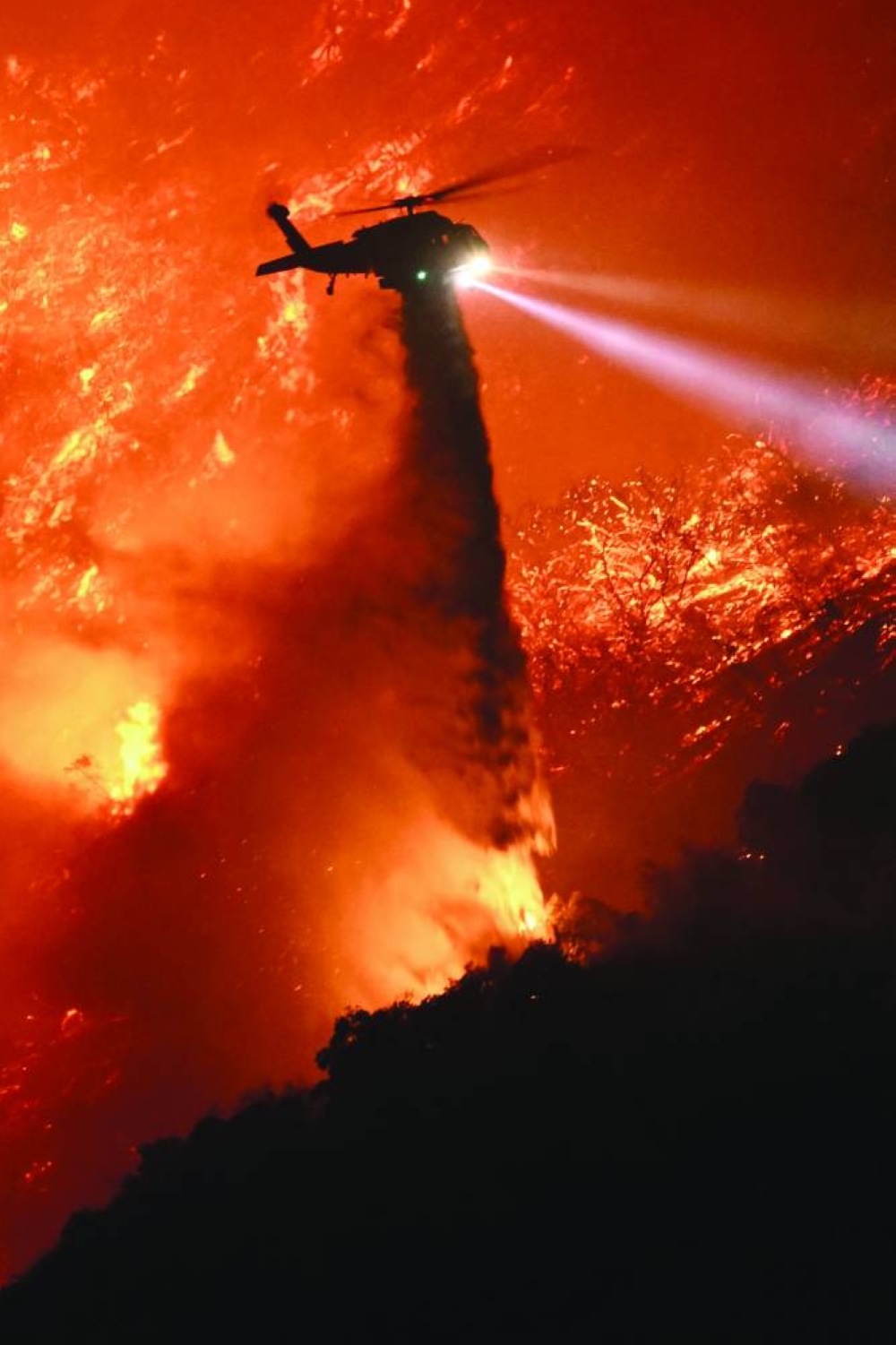 A firefighting helicopter drops water as the Palisades fire grows near the Mandeville Canyon neighbourhood and Encino, California. – AFP