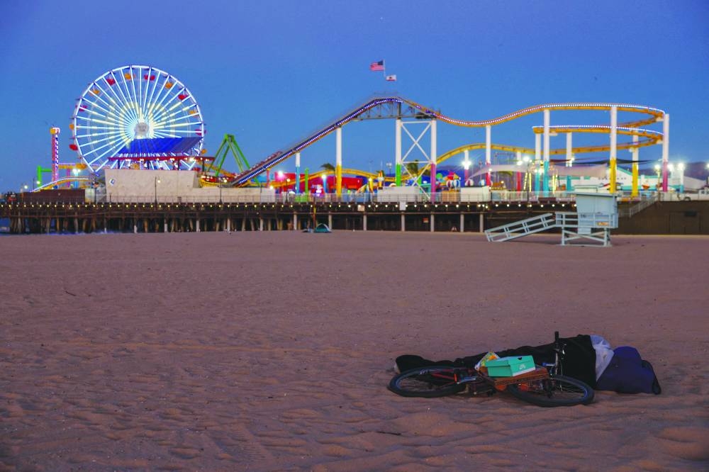 A person sleeps on the beach in front of a ferris wheel displaying a message as a tribute to the victims of the California wildfires, at the Santa Monica Pier in Santa Monica, California. – Reuters