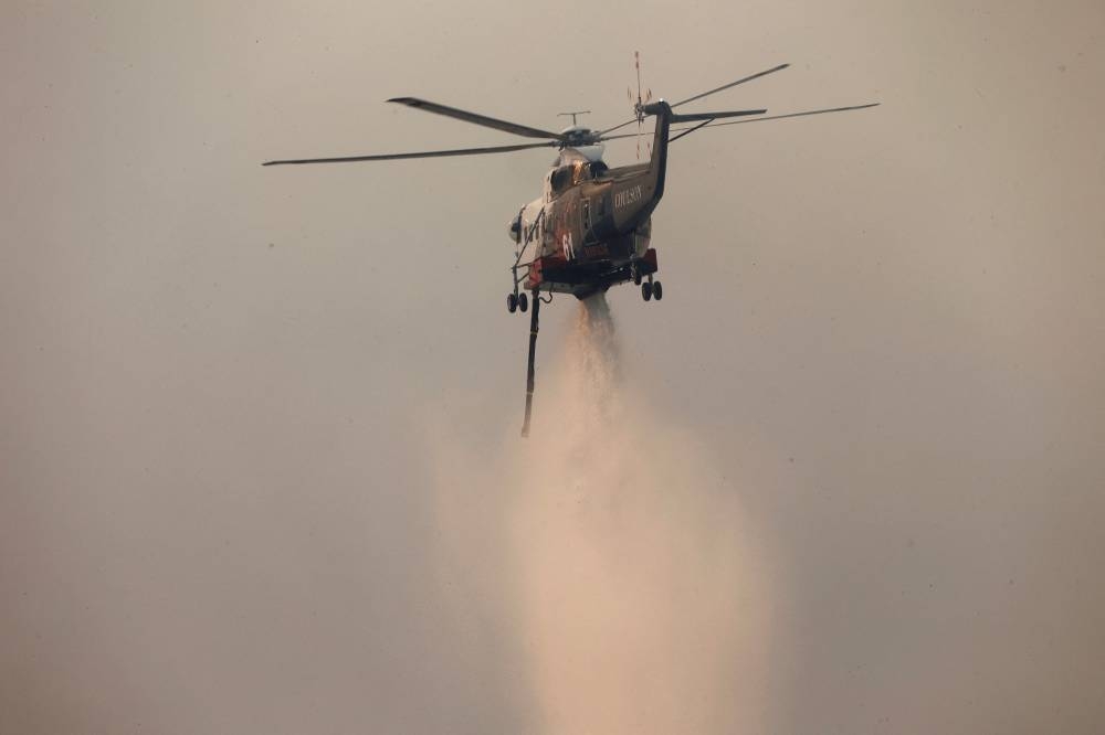 A helicopter drops water on the Palisades Fire, one of several simultaneous blazes that have ripped across Los Angeles County, along Mandeville Canyon, in the Encino neighborhood of Los Angeles, California, on Saturday. REUTERS. 