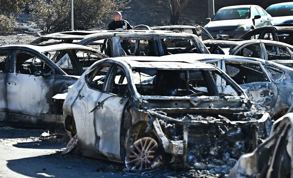 A police officer inspects destroyed vehicles left along Sunset Boulevard during the January 7 evacuation from the Palisades Fire, in Los Angeles, California, on Sunday. AFP
