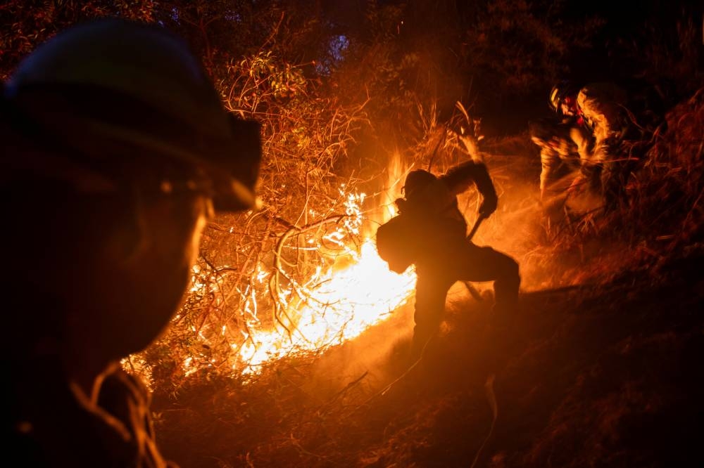 Firefighters extinguish a fire as the Palisades Fire, one of several simultaneous blazes that have ripped across Los Angeles County, burns in Mandeville Canyon, a neighborhood of Los Angeles, California, on Sunday. REUTERS