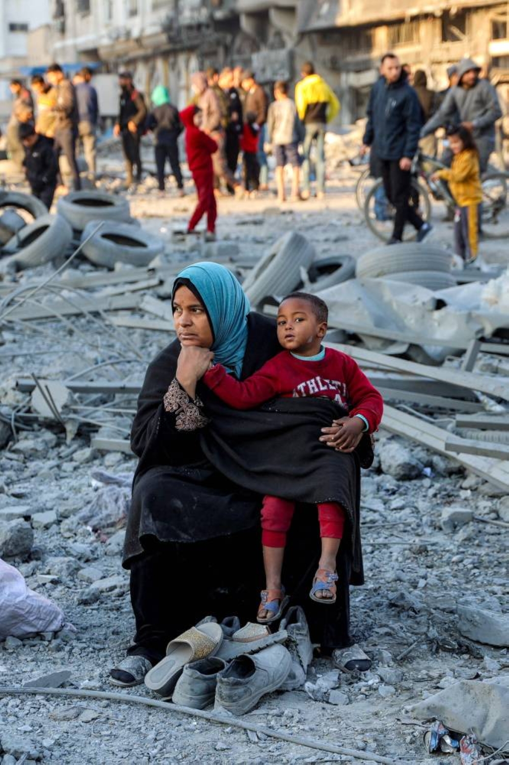 A woman sits with a child with salvaged footwear amidst debris and rubble at the site of Israeli bombardment on a residential block in Jalaa Street in Gaza City, on Tuesday. AFP